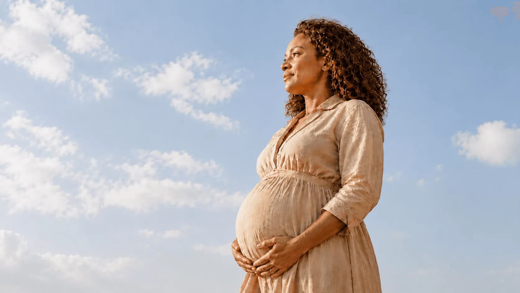 Surrogate mother cradling her belly outdoors under a clear blue sky